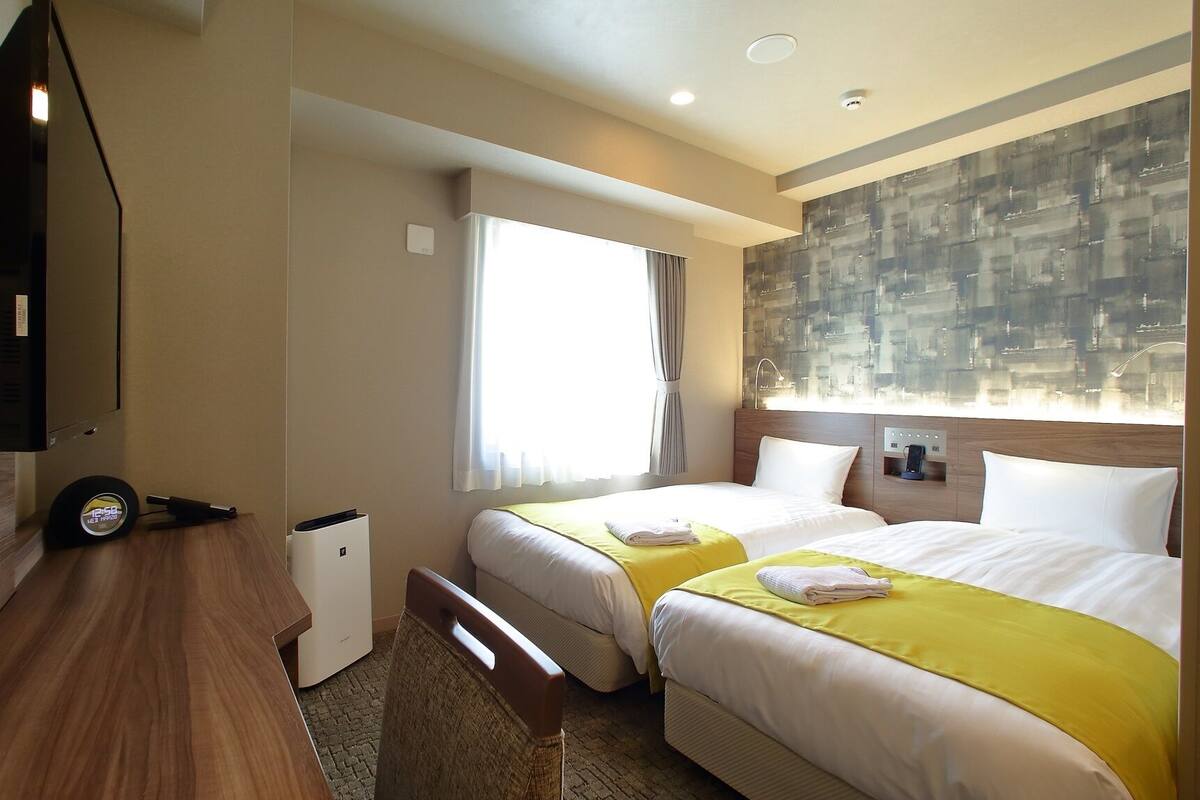 A hotel room with two beds, a desk, a TV, and a cityscape view.