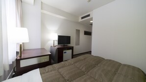 Een hotelkamer met een bed, een bureau met een televisie, een lamp en een kleine koelkast.