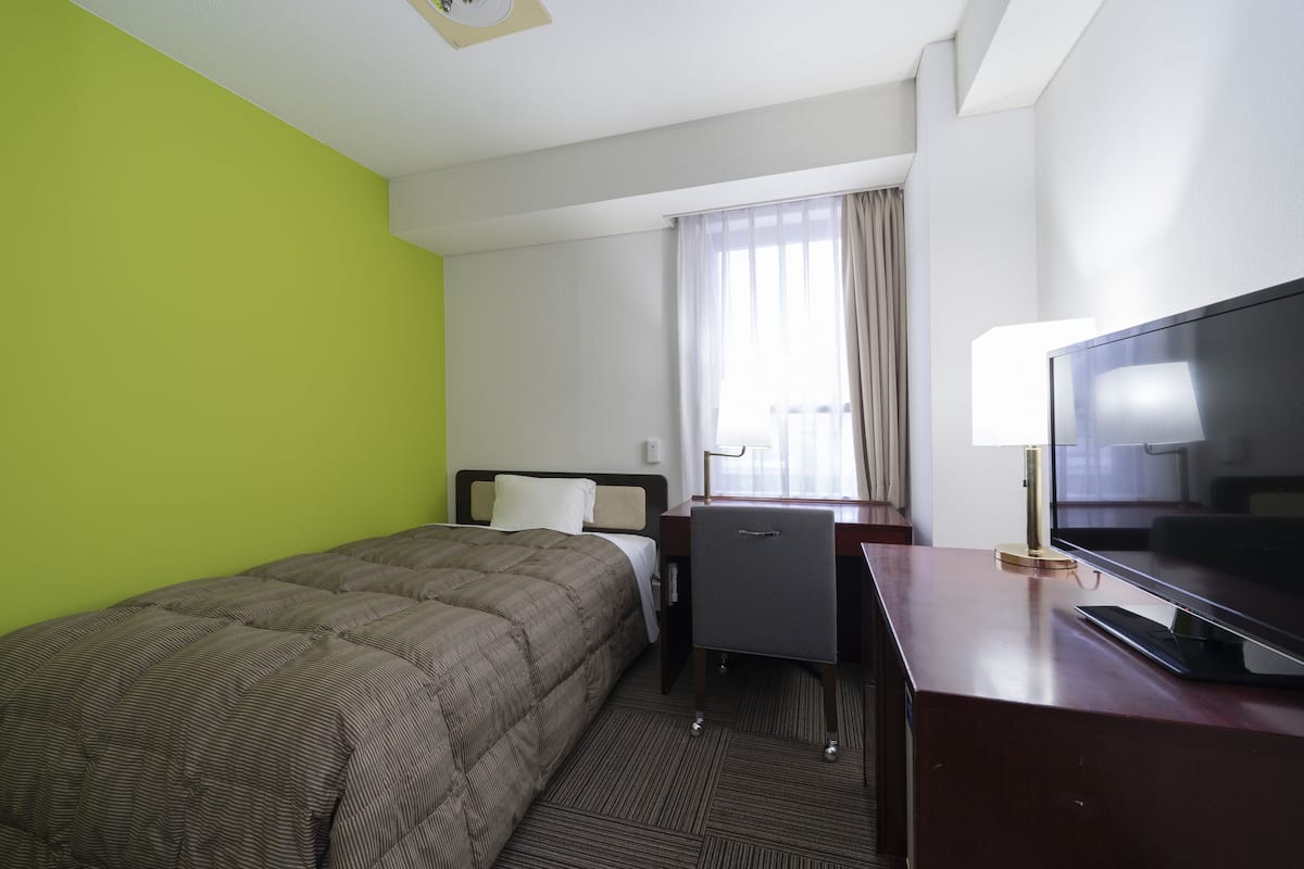 Una habitación de hotel con cama, escritorio con televisor, silla y ventana con cortinas.