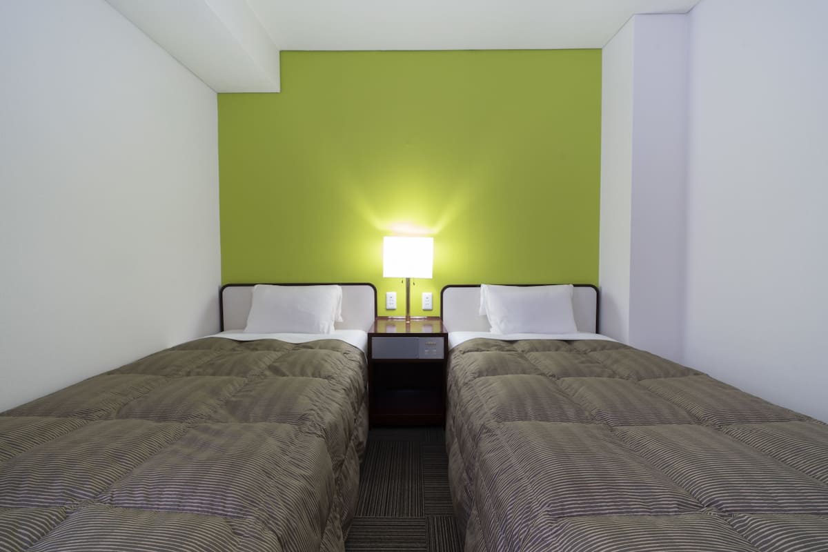 Habitación de hotel con dos camas individuales, una mesita de noche con lámpara y una pared de acento verde.