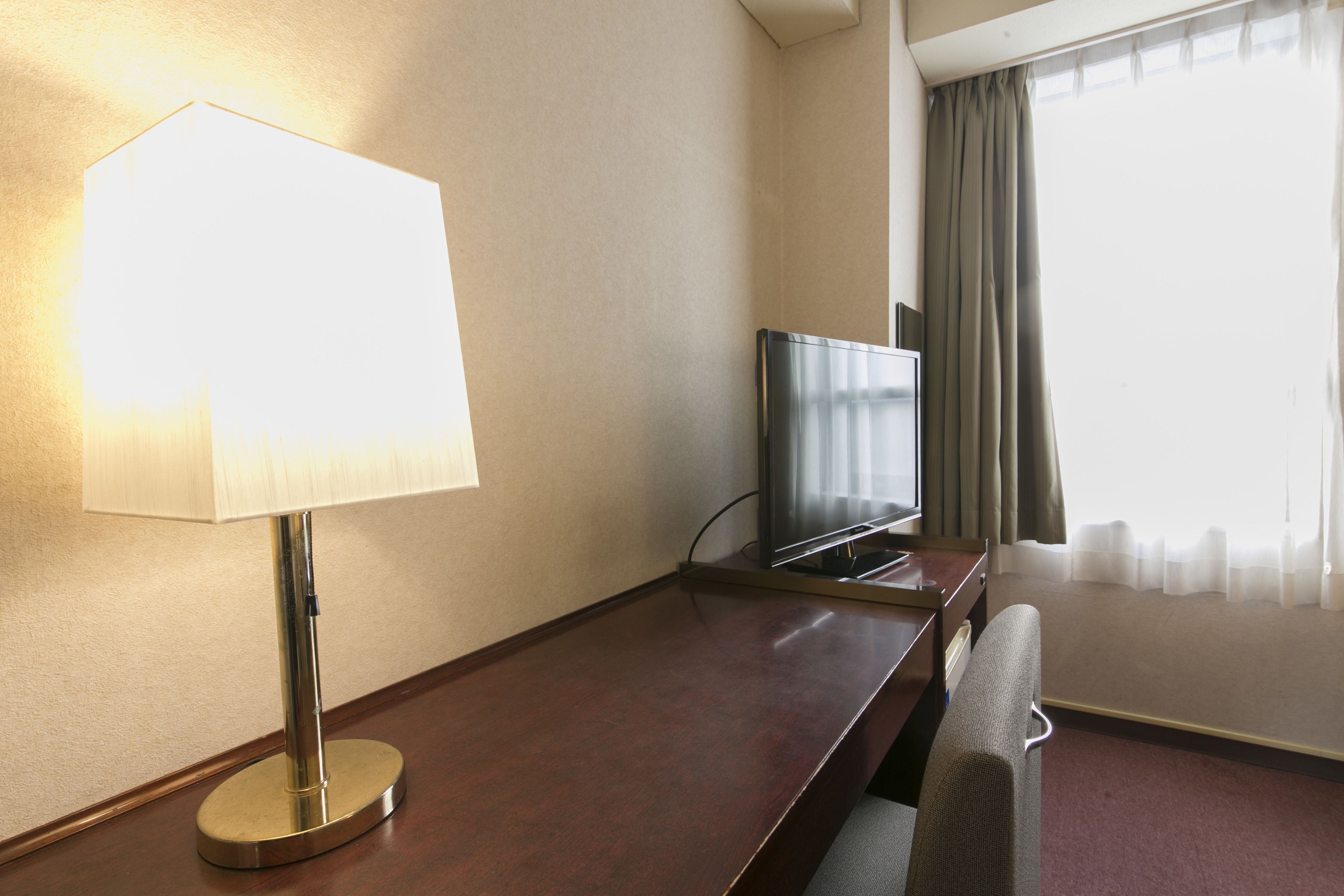 Ein Hotelzimmer mit einem Holztisch, einem Fernseher, einer Lampe und einem Fenster mit Vorhängen.