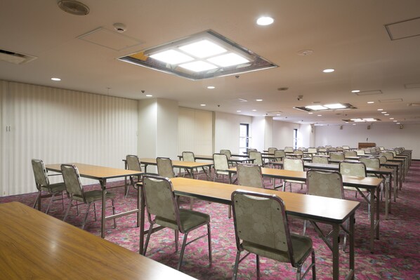 Une salle de conférence dotée de plusieurs tables et chaises, d’un tapis à motifs et d’un plafond équipé d’un éclairage encastré et d’une lucarne.