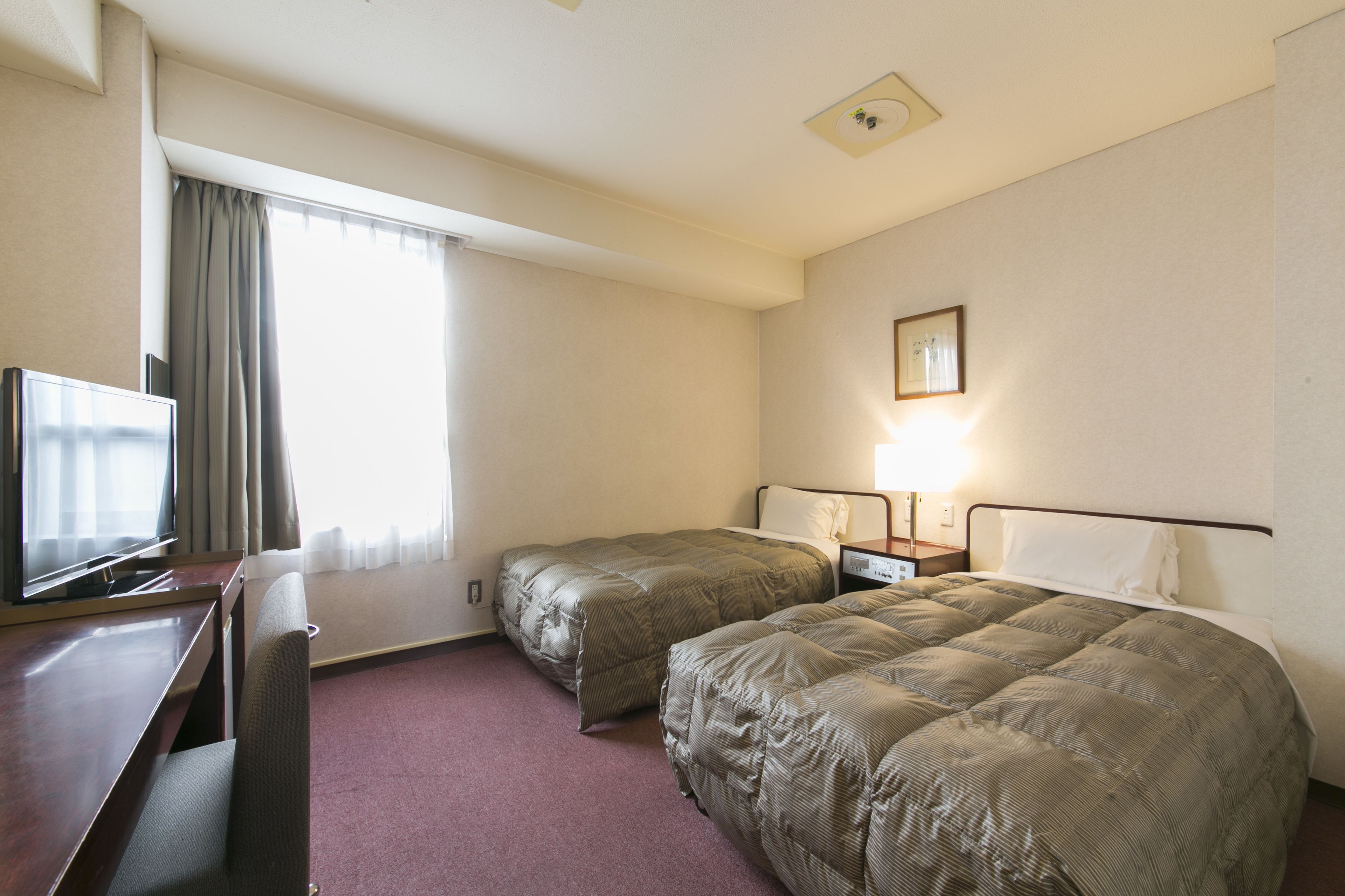Habitación de hotel con dos camas, un escritorio, un televisor y una ventana con cortinas.