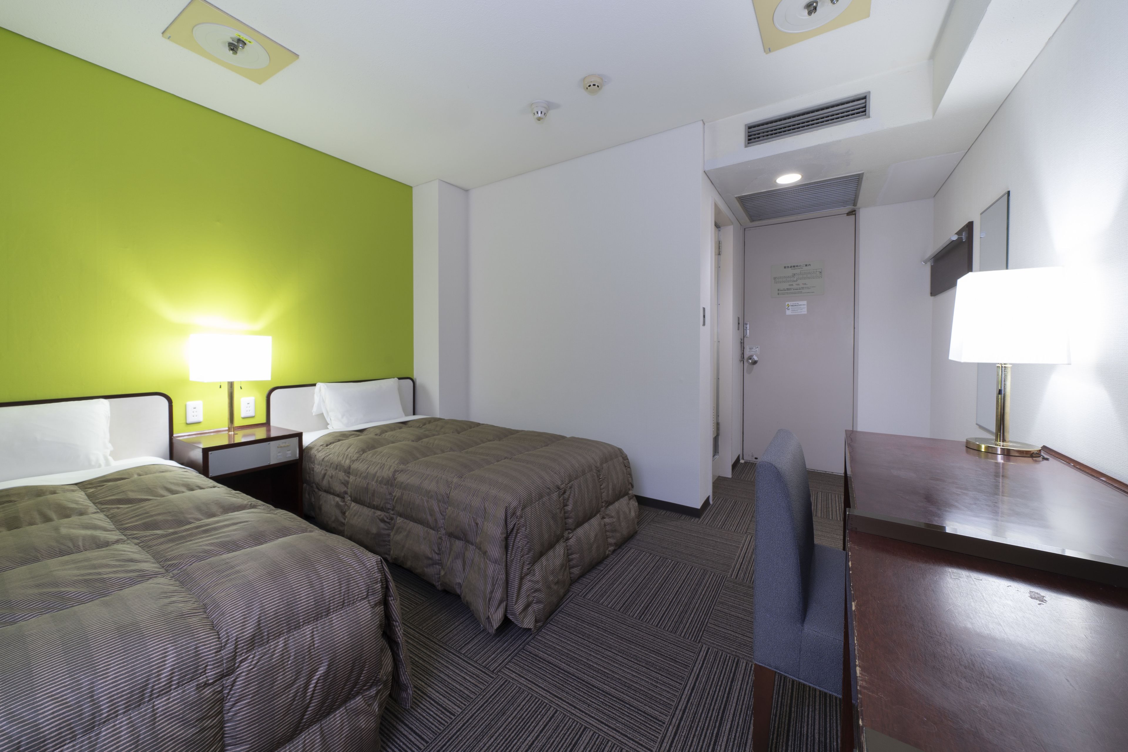 Una camera d'albergo con due letti, una scrivania, una sedia e una lampada.