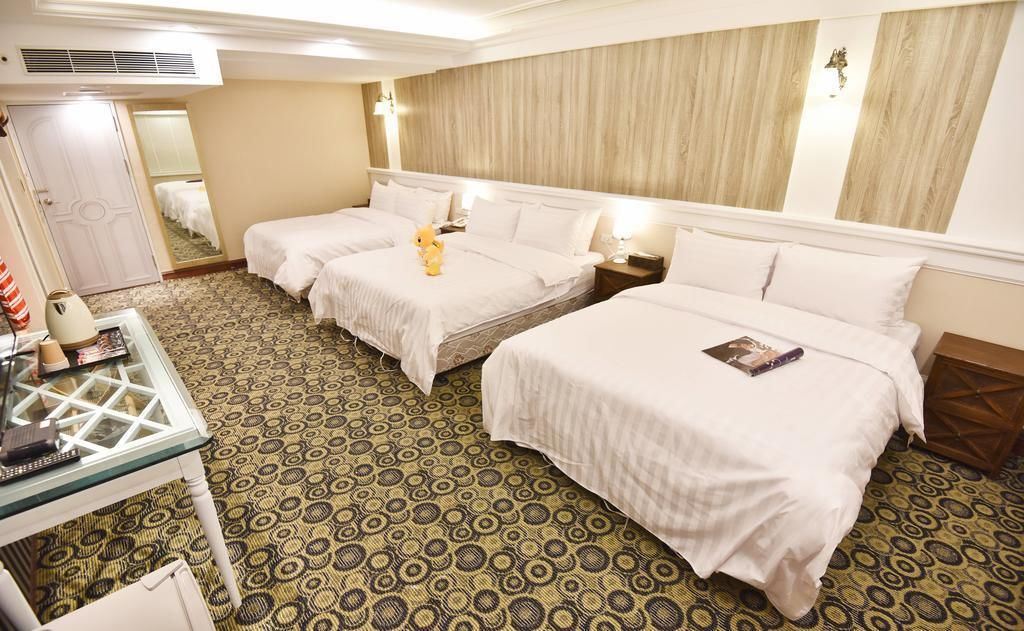 A hotel room with two beds, a small table with a lamp, and a patterned carpet.