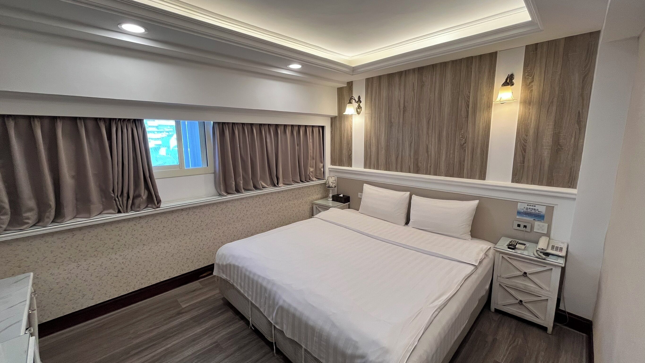 A hotel room with a large bed, a nightstand with a phone, and a window with curtains.
