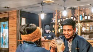 Un bar aux murs et aux étagères en bois, où sont exposées de nombreuses bouteilles d’alcool.