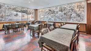 Un restaurant doté de grandes fenêtres donnant sur un paysage enneig é. Les tables sont disposées avec des chaises, et le sol est recouvert de carreaux formant un motif.