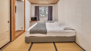 Une chambre à coucher avec un lit, une table de chevet, une télévision et une fenêtre avec des rideaux.