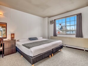 Ein Schlafzimmer mit Bett, Nachttisch, Lampe, Fenster mit Vorhängen und Heizkörper.