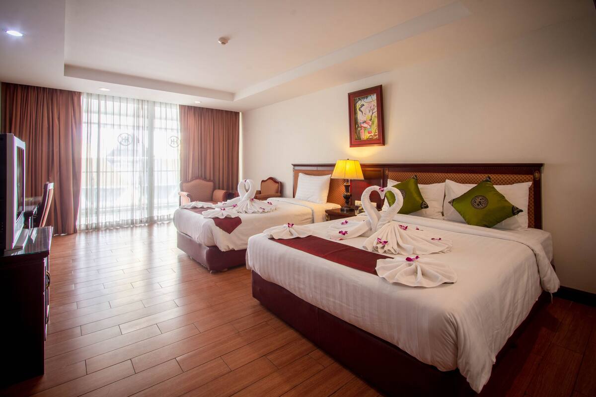A hotel room with two beds, a television, and a large window with curtains.