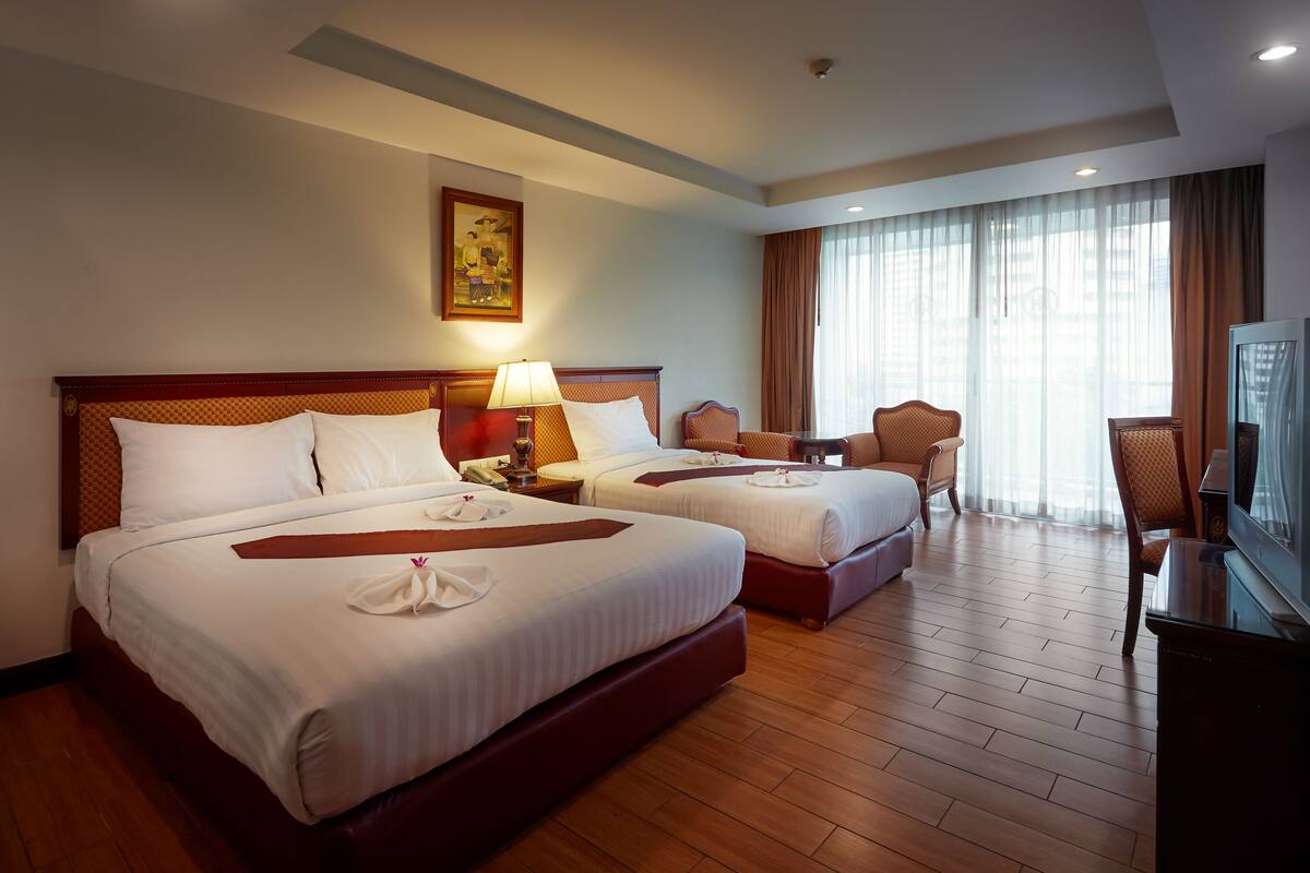 A hotel room with two beds, a desk, a chair, and a television.