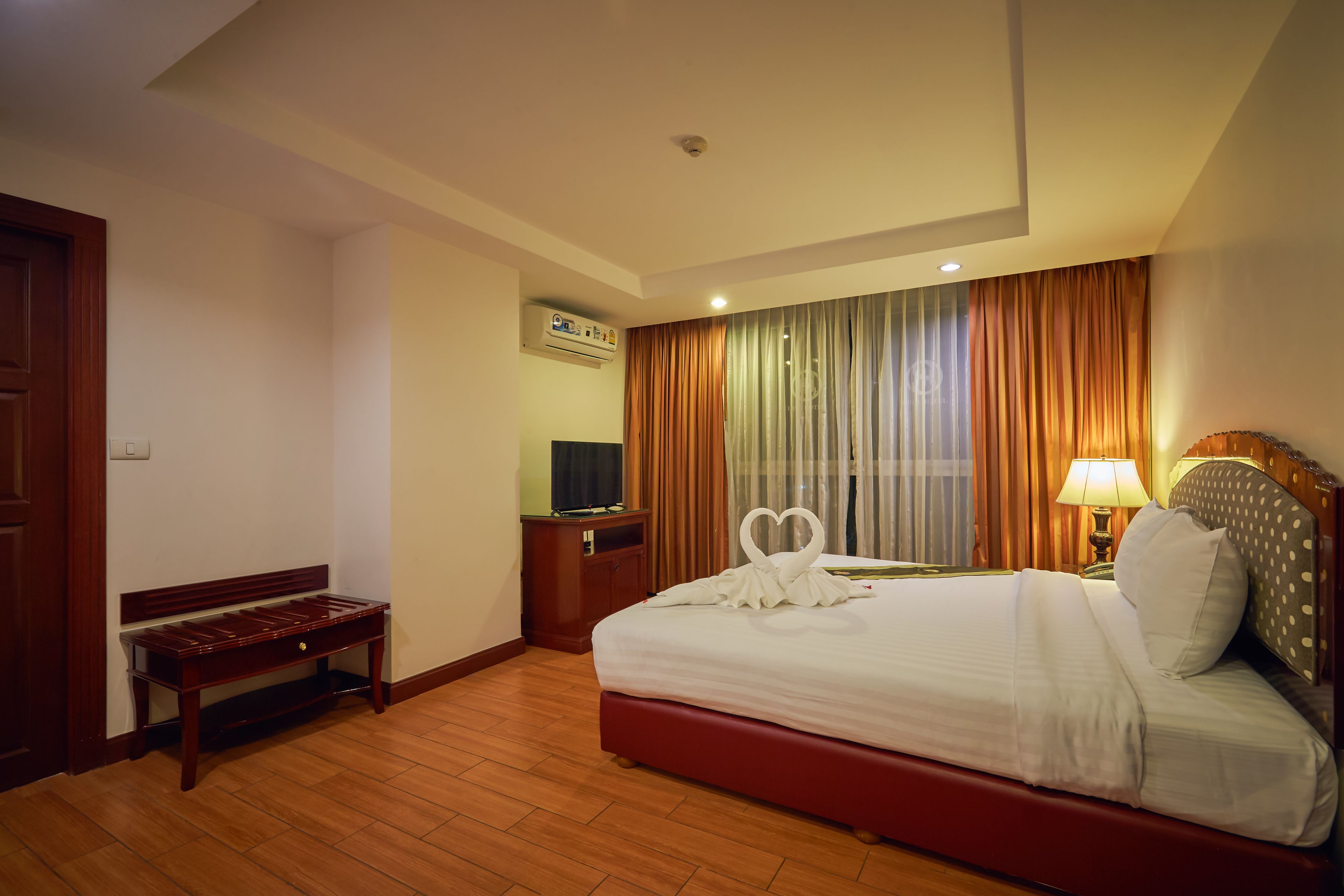 Habitación de hotel con cama, una banca, escritorio, televisor y aire acondicionado.