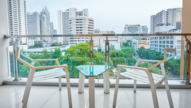 A balcony with a glass table and two chairs, offering a city view. - Nana Hiso Hotel (Bangkok)