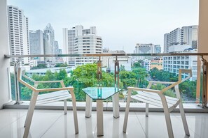 A balcony with a glass table and two chairs, offering a city view. - Nana Hiso Hotel (Bangkok)