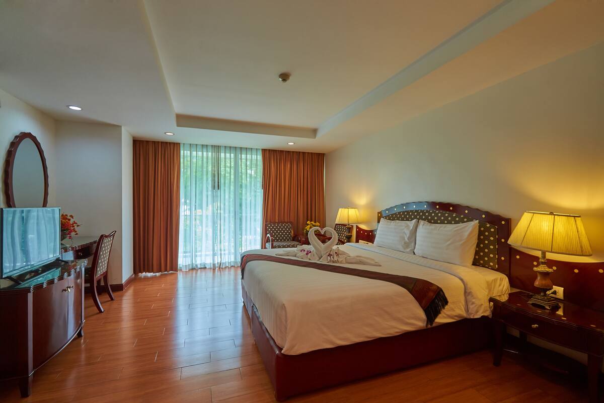 A hotel room with a large bed, a desk with a chair, a TV, and a window with curtains.