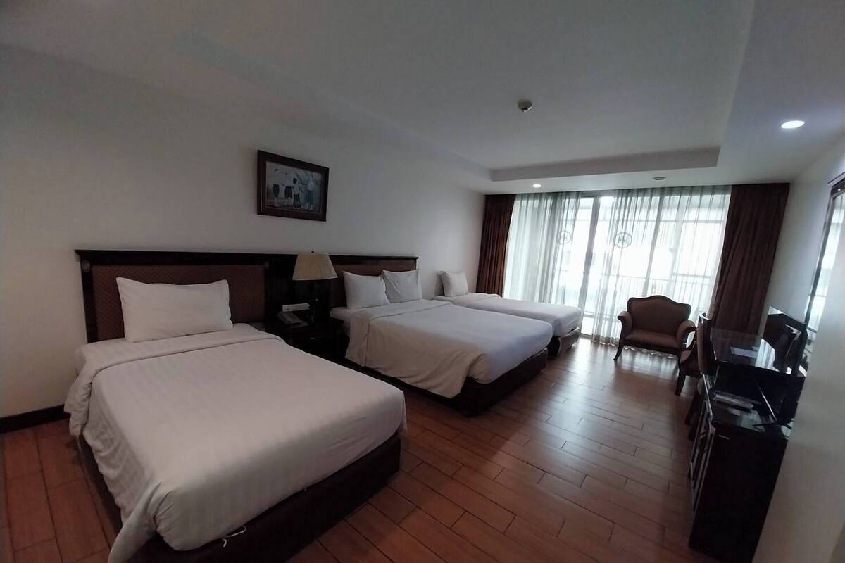 A hotel room with two beds, a desk, a chair, and a large window with curtains.