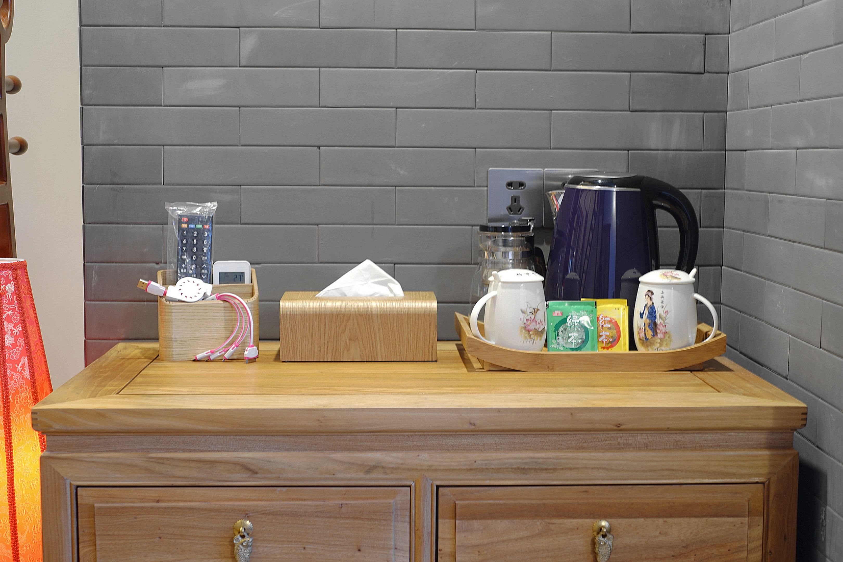Una encimera de madera con una caja de pañuelos, un control remoto, un hervidor y una bandeja con tazas de té y cajas.