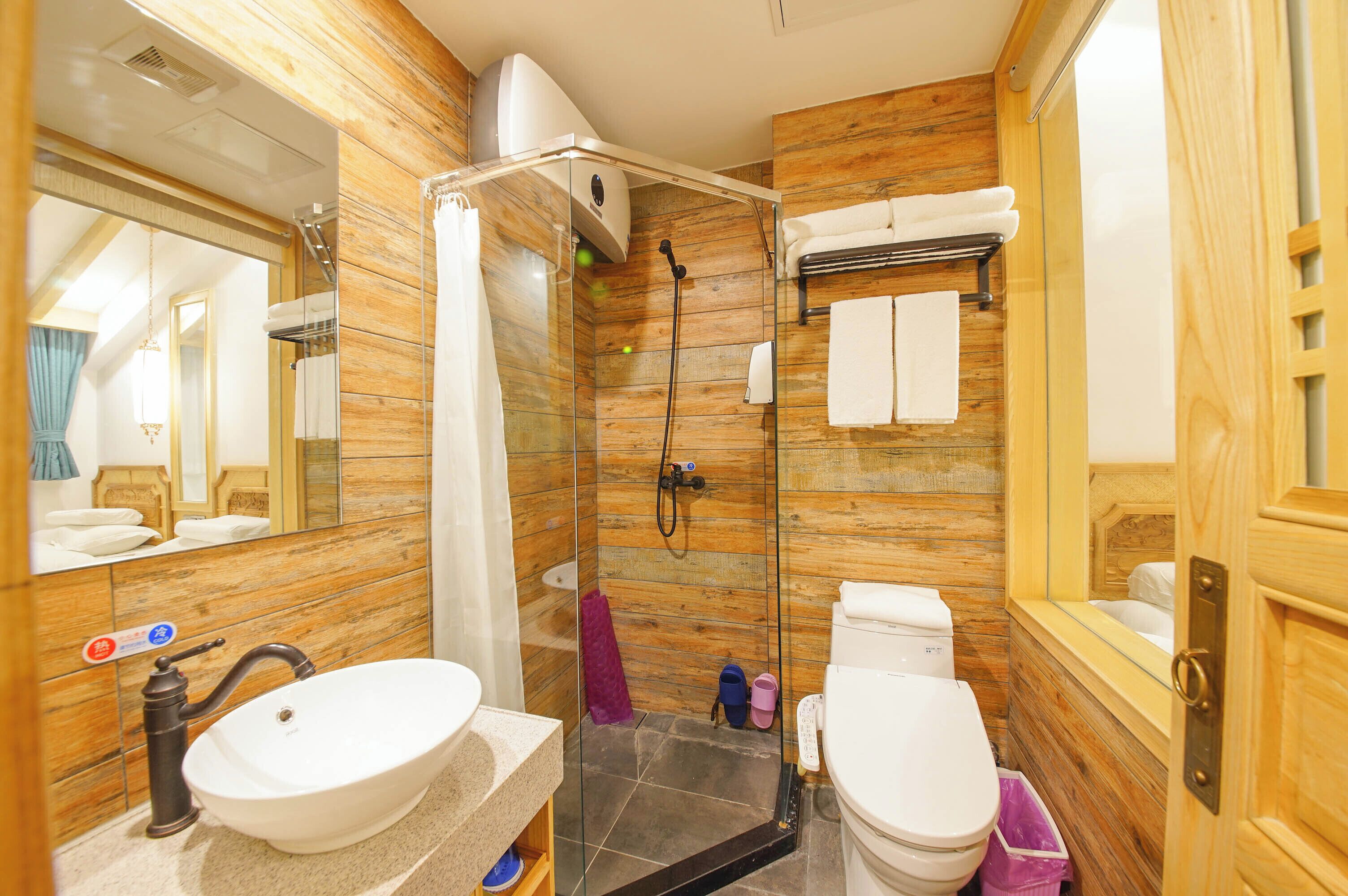 Ein Badezimmer mit Holzwandgestaltung, einer gläsernen Duschkabine, einem weißen Waschbecken und einer Toilette.