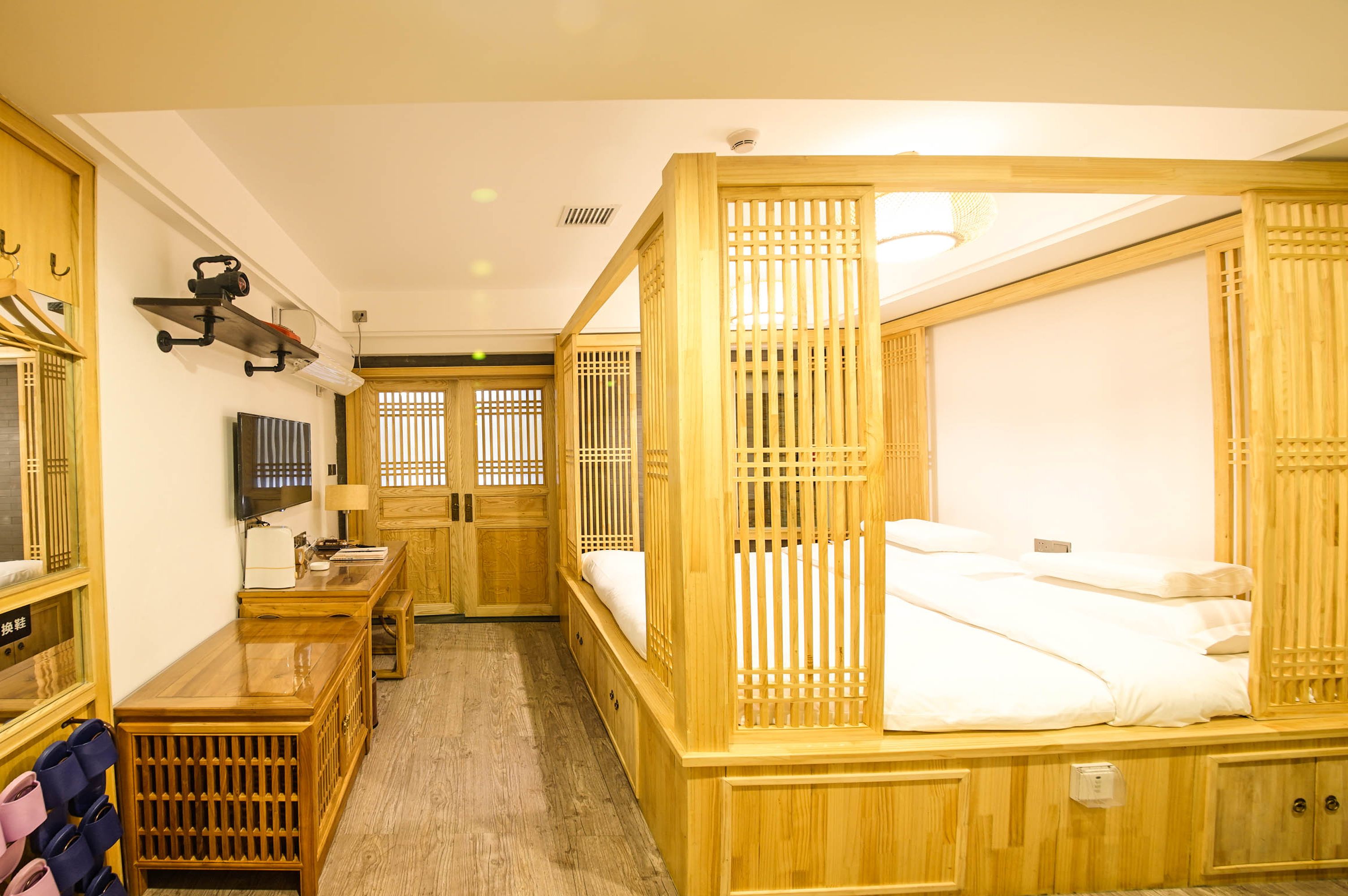 Una habitación tradicional japonesa con cama de madera, televisor, escritorio y armario.