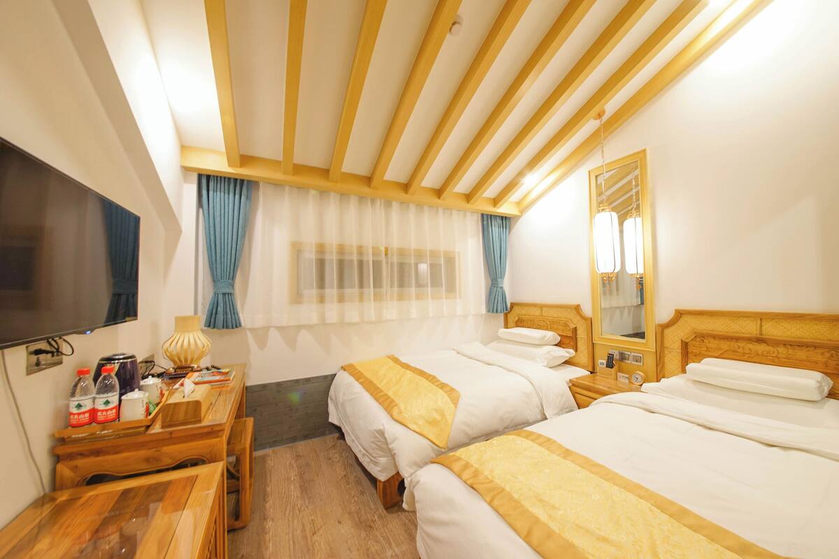 Una habitación de hotel con dos camas, un escritorio de madera, televisión y ventana con cortinas.