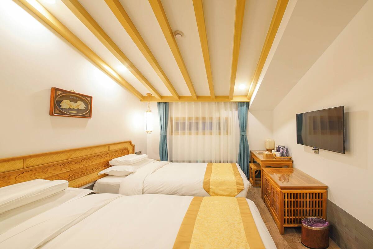 Habitación de hotel con dos camas, cabecera de madera, televisor, escritorio con lámpara y un cubo de basura.