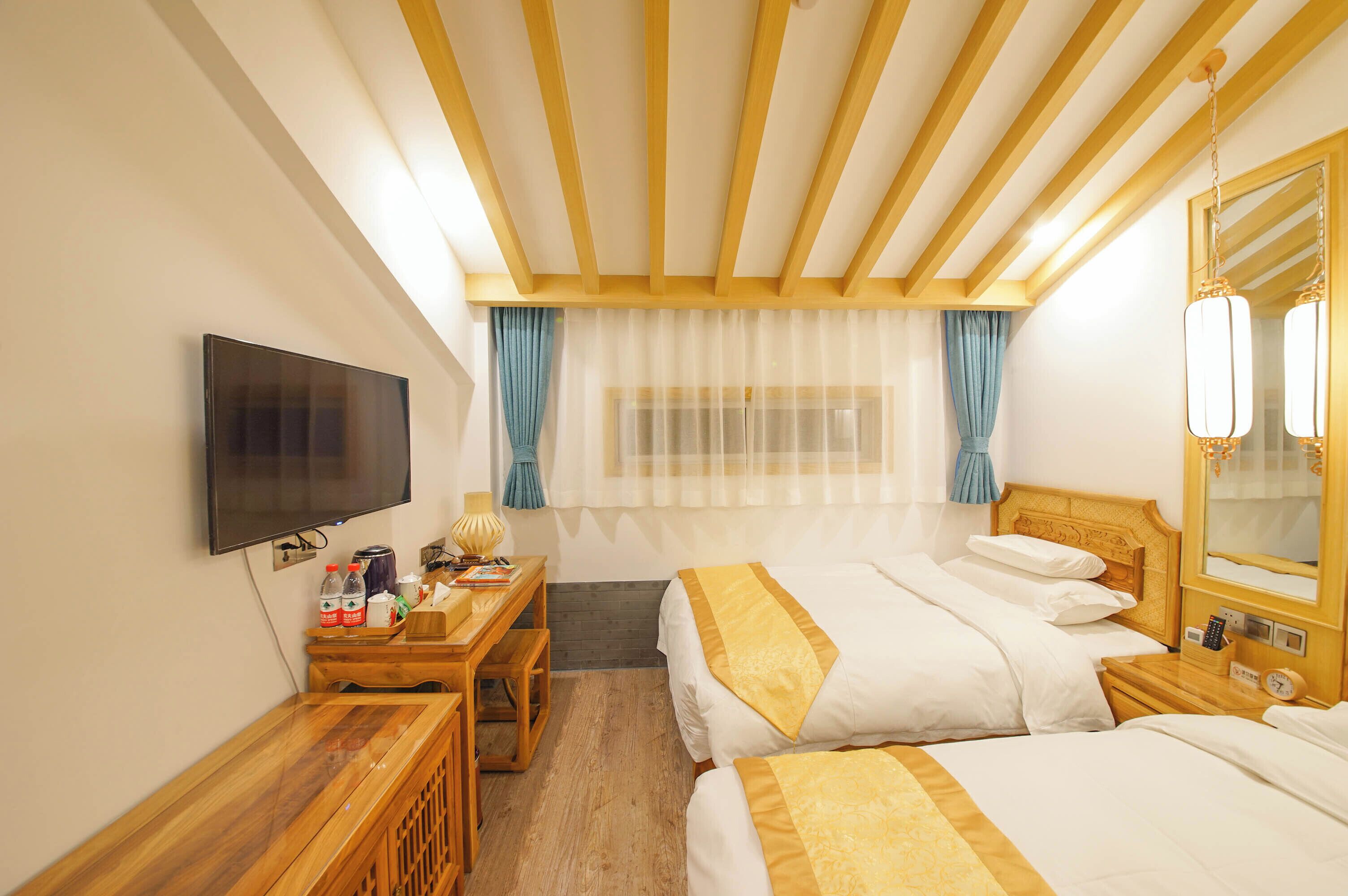 Habitación de hotel con dos camas, un escritorio con silla, televisor y techo de madera.