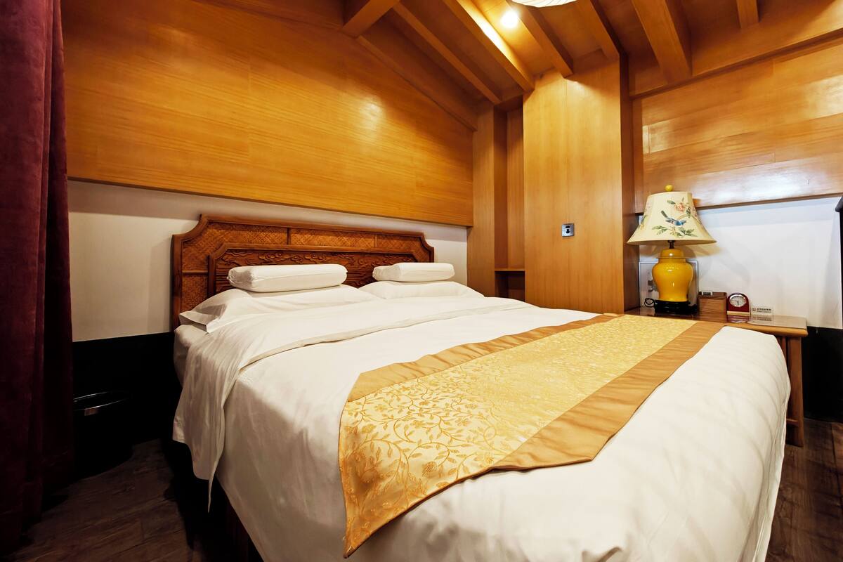 Una habitación de madera con una cama grande, una mesita de noche con lámpara y techo de madera.