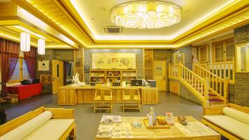 A spacious lobby with a wooden reception desk, seating area, and a staircase.