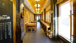 A corridor with wooden benches and tables, a decorative ceiling, and a large window on the right. - Datong Pipa Hotel (Datong)