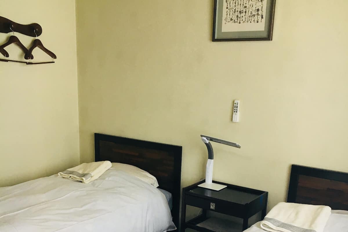Two single beds with white linens, a nightstand with a lamp, and a framed picture on the wall.