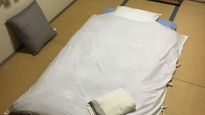 A room with tatami flooring, a bed with white bedding, a grey pillow, and a wooden cabinet.