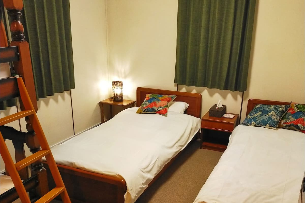 A room with two single beds, a wooden ladder, a bedside table with a lamp, and a nightstand with a tissue box.