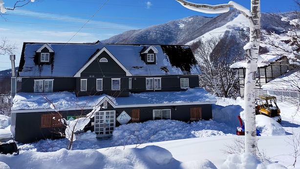 A large, dark-colored building with a steep roof, surrounded by snow-covered ground and trees.