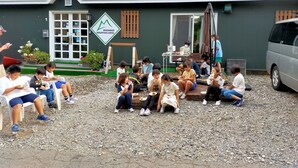 A group of people seated on outdoor benches in front of a building with a sign reading "Madarao Mountain Lodge".