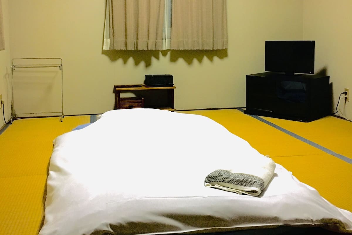 A hotel room with a bed, a television, a small table, and a window with curtains.