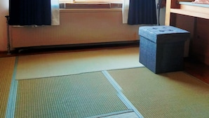 A room with tatami mats, a window with curtains, a heater, and a small stool.
