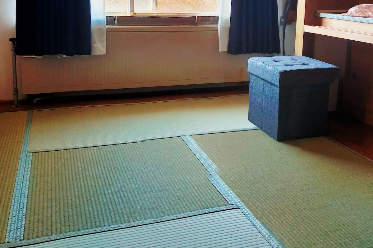 A room with tatami mats, a window with curtains, a heater, and a small stool.