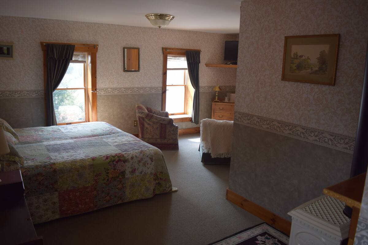A bedroom with a bed, a chair, a dresser, and a window with curtains.