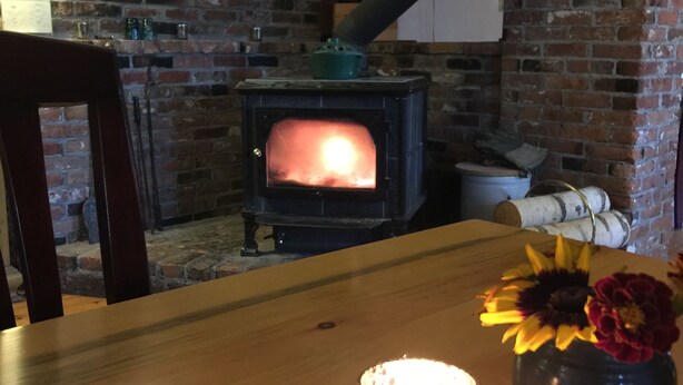 Ein rustikaler Raum mit Backsteinwand, Holztisch, einer brennenden Kerze und einem Blumenstrauß in einer Vase.
