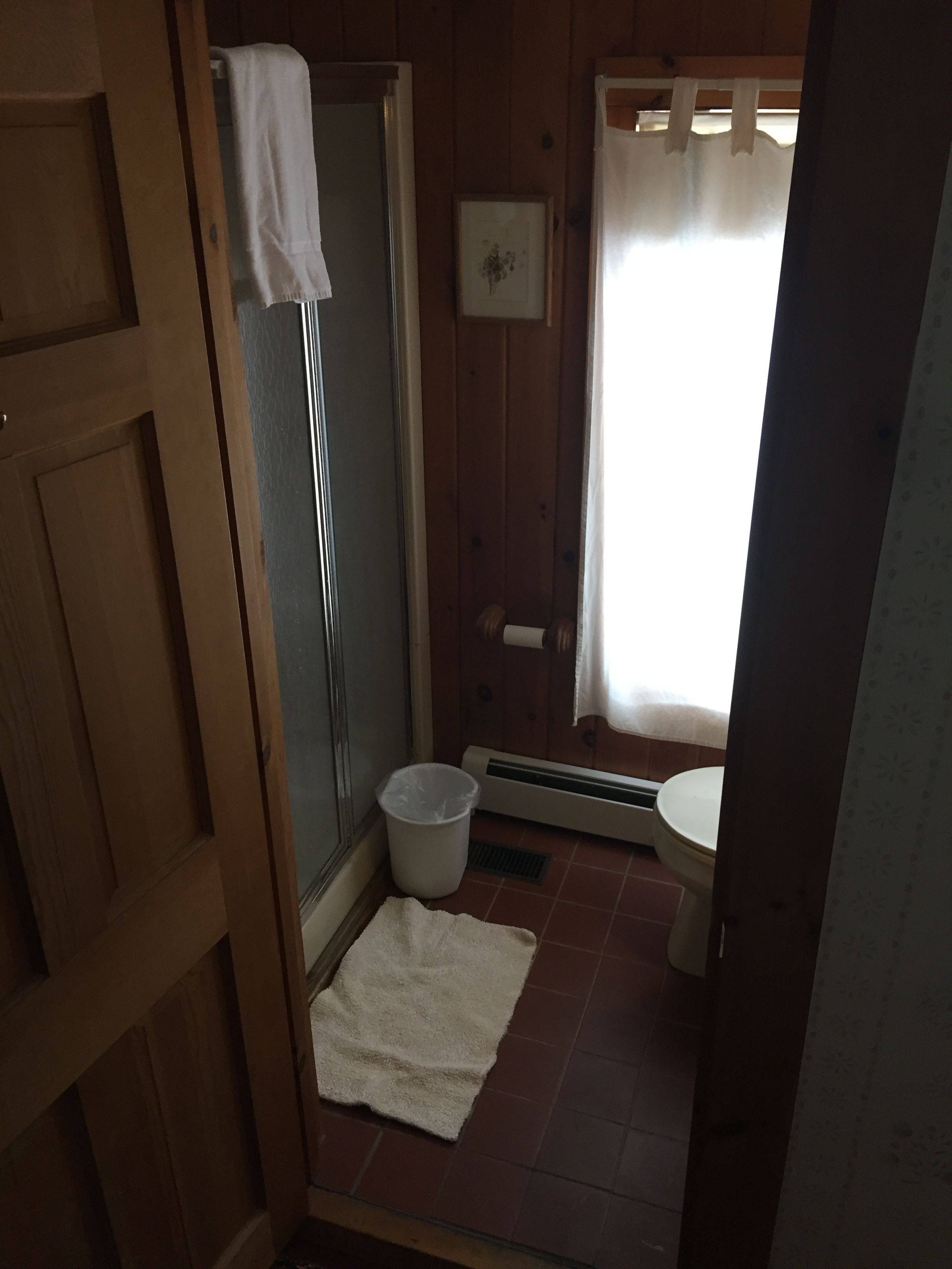 A wooden-paneled bathroom with a shower, toilet, and a towel rack.