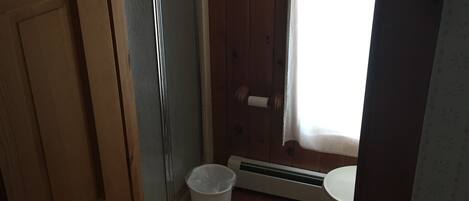 A wooden-paneled bathroom with a shower, toilet, and a towel rack.