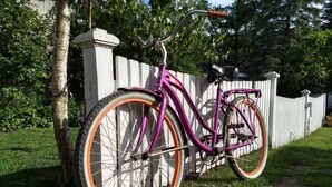 Ein violettes Fahrrad steht an einem weißen Zaun in einer grünen Wiese.
