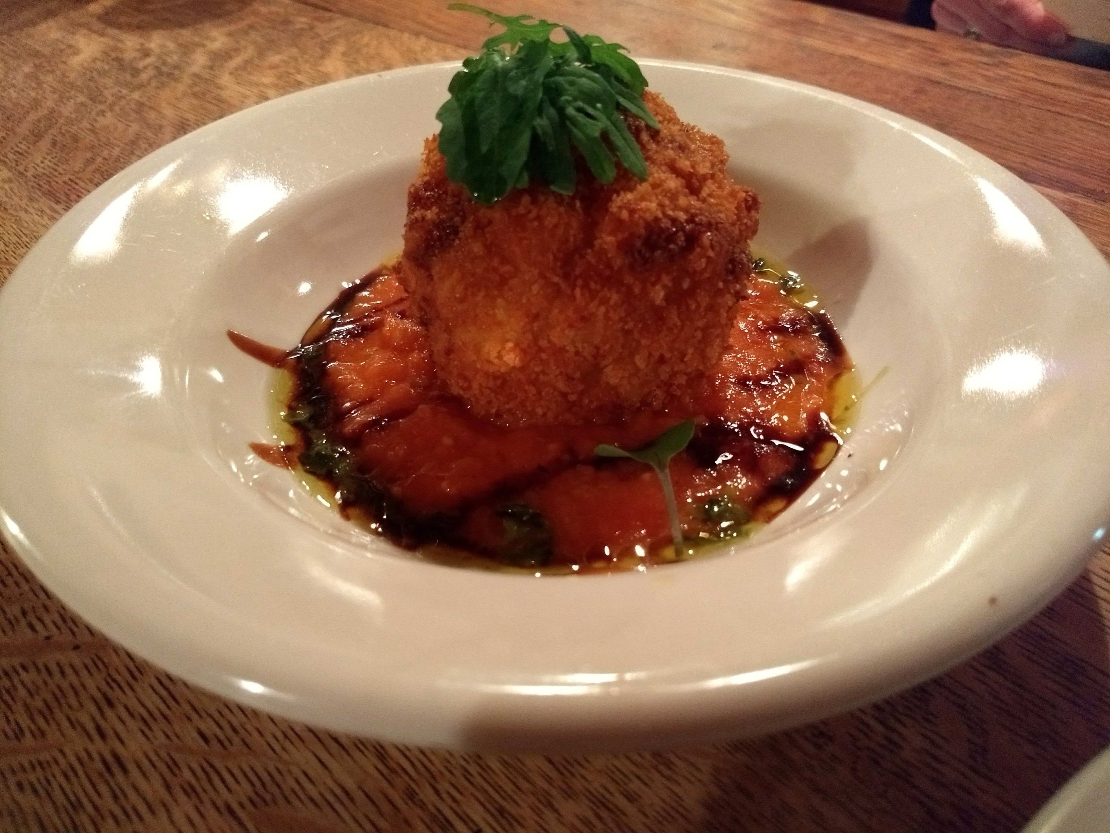 Un plato blanco con un alimento, posiblemente pescado o carne, decorado con hojas verdes, sobre una mesa de madera.