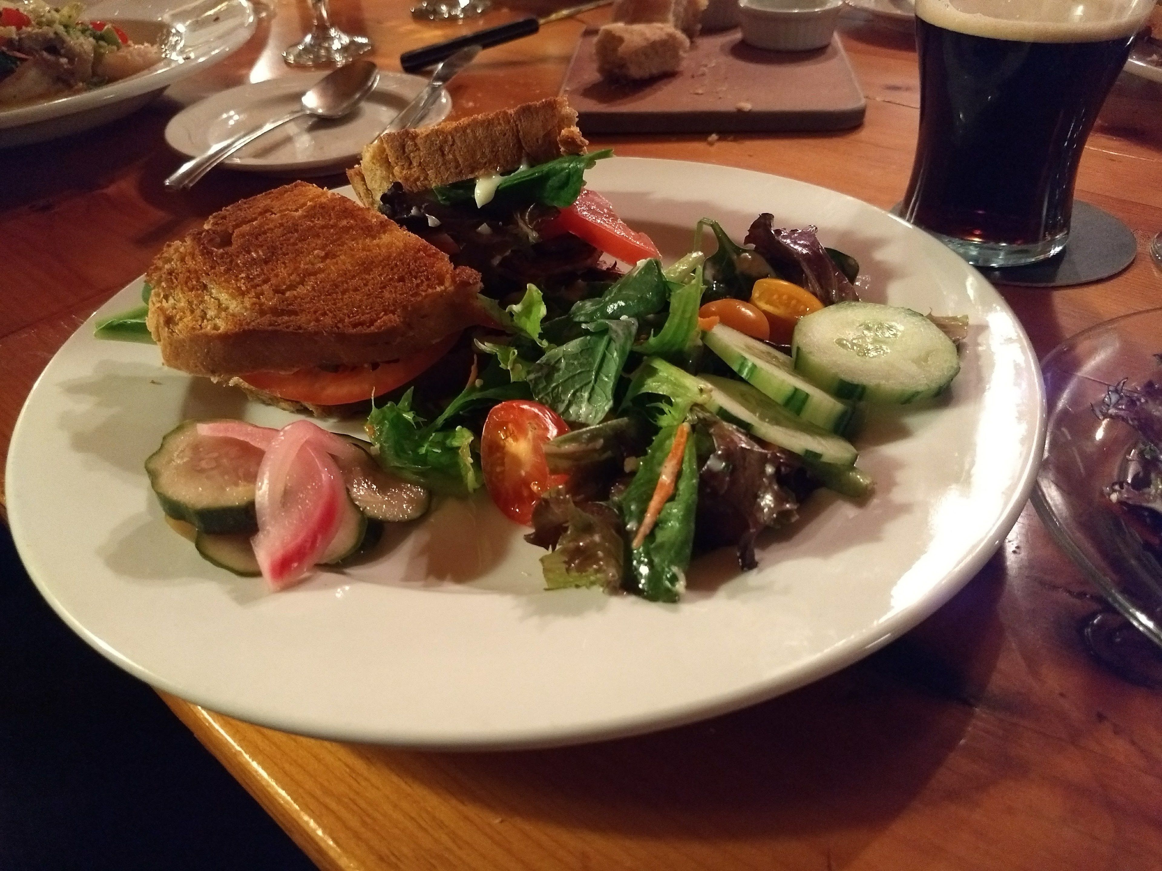 Une assiette avec un sandwich, une salade et un verre de bière, le tout posé sur une table en bois.