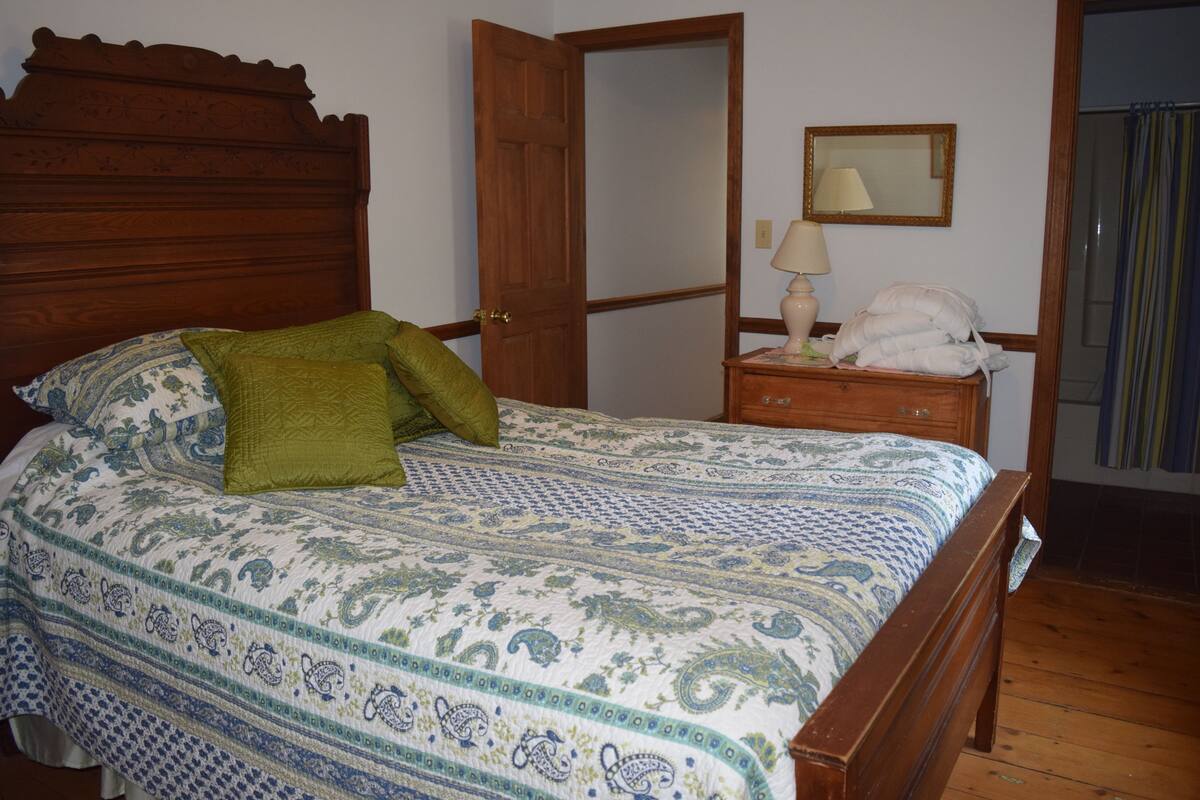 A bedroom with a wooden bed, a nightstand with a lamp, and a mirror on the wall.