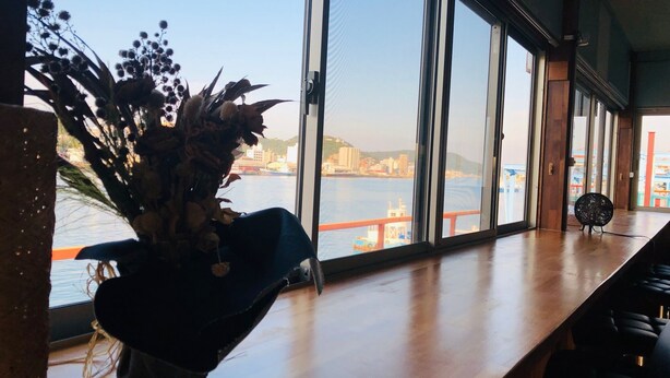 A bar area with a large window overlooking a waterfront, a vase with dried flowers, and a chair. - Seaside Hostel LightHouse (Onomichi)