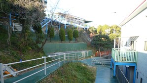 A multi-level outdoor staircase with metal railings, surrounded by greenery and a building in the background. - Seaside Hostel LightHouse (Onomichi)