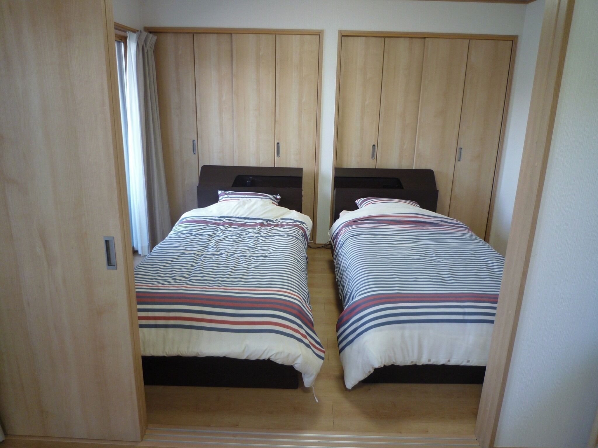 A bedroom with two single beds, wooden wardrobes, and a window with curtains.