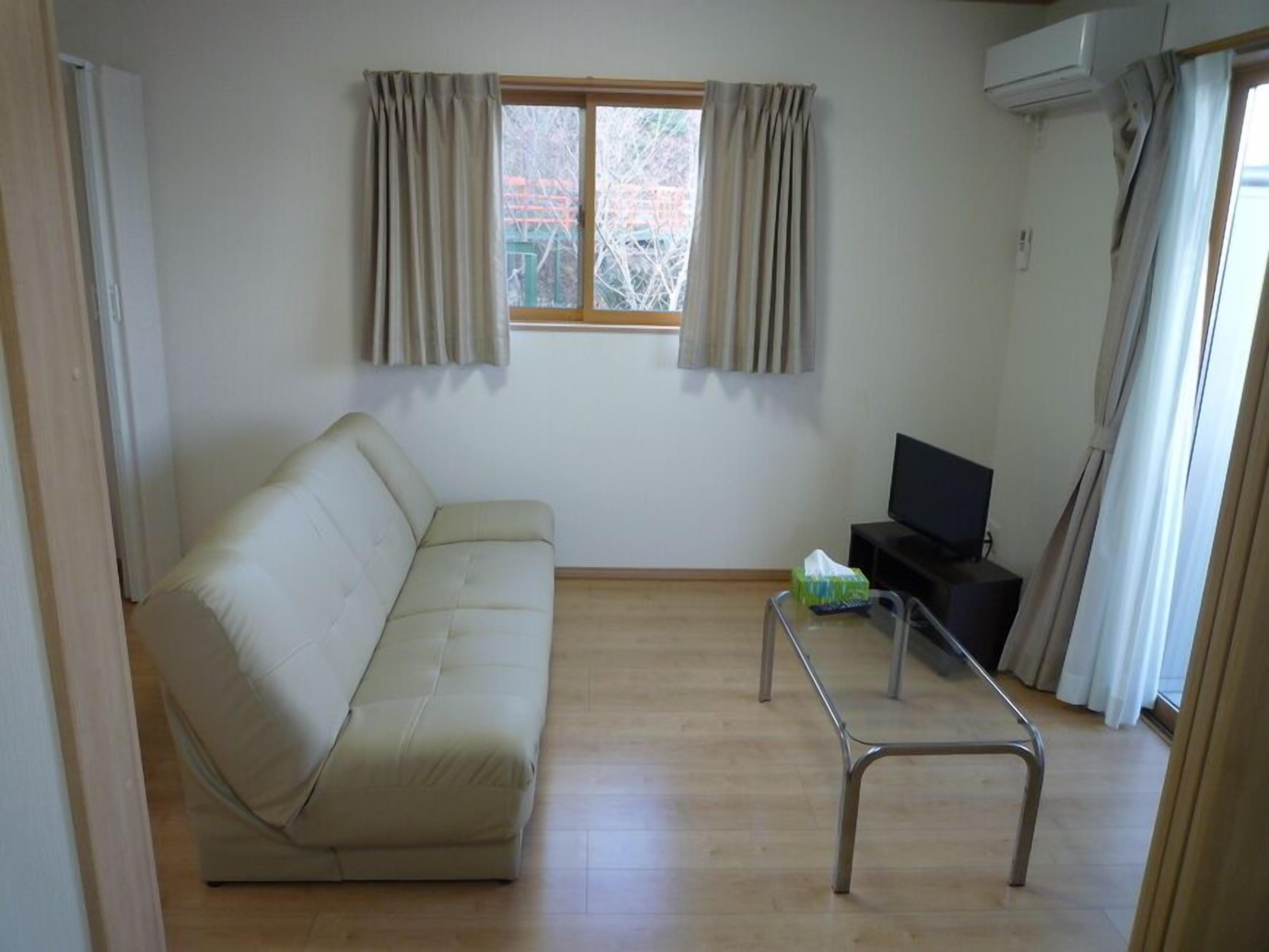 A room with a sofa, a TV, a small table, and a window with curtains.